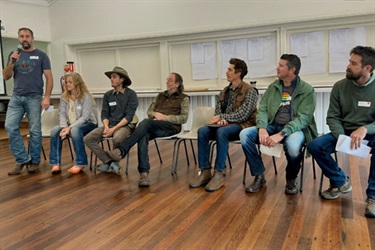 A row of people sitting on chairs with one person speaking