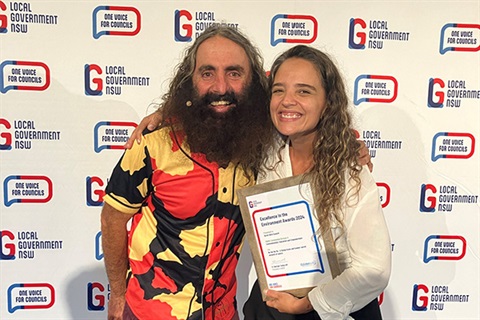 Man and lady hugging and holding award saying Excellence in environment