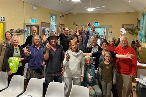 16 people in room holding portable transmitters looking happy