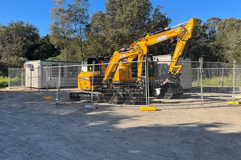 large earthmover behind security fence with site office in background